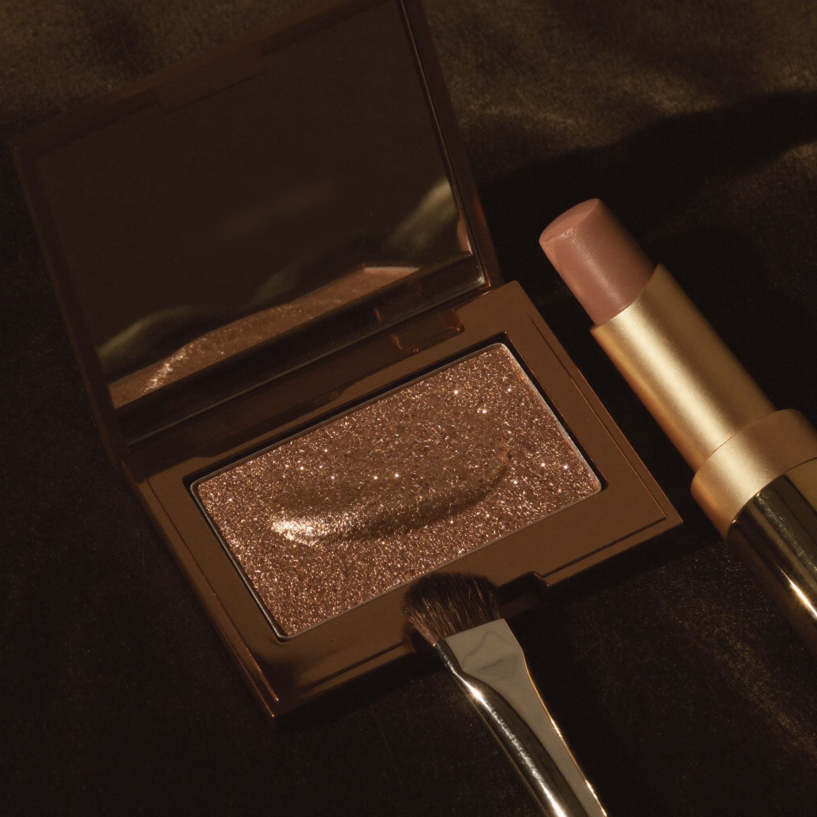 Bronze highlighter and a nude lipstick on dark velvet